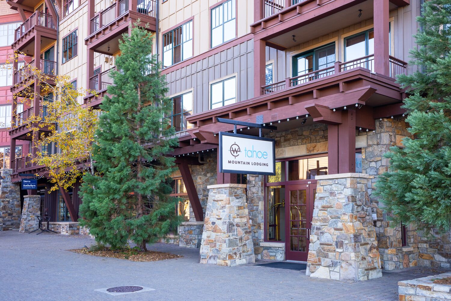 Un immeuble à plusieurs étages avec une façade en pierre, une enseigne indiquant « Tahoe Mountain Lodge », et une entrée bien visible.
