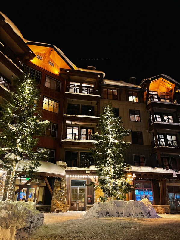 Un hotel de varios pisos con fachada de piedra, balcones y ventanas iluminadas.