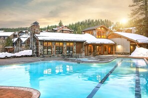 Un resort con piscina, edificios de piedra y techos nevados.