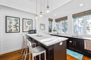 Una cocina moderna con armarios blancos, una isla de mármol, luces colgantes y obras de arte en las paredes.