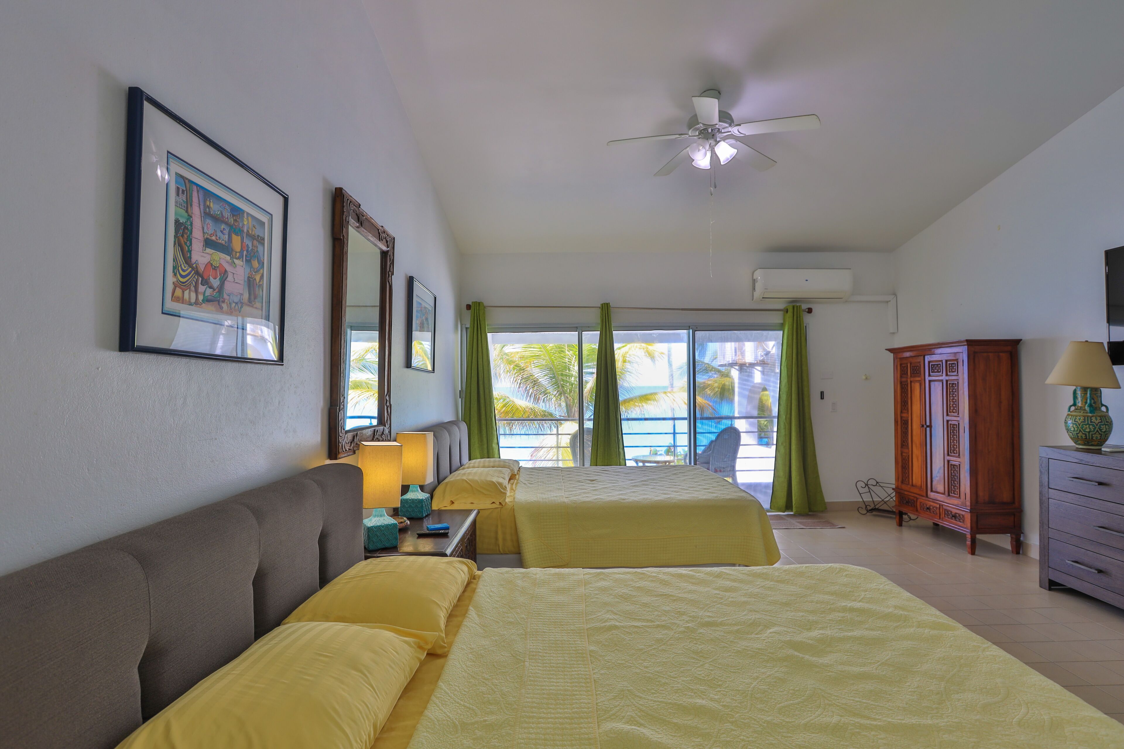 A hotel room with two beds, a ceiling fan, a large window with curtains, a wooden cabinet, and a television.