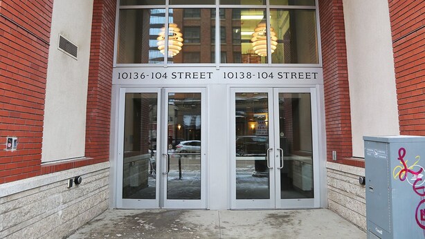 A building entrance with double doors, a visible fire exit sign, and a mailbox on the right. - Heart of Downtown Edmonton, walking distance to Rogers Place / LRT station  (Edmonton)