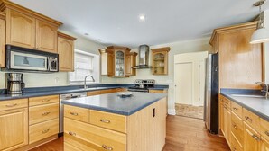A spacious kitchen with wooden cabinets, a central island, stainless steel appliances, and a large window.