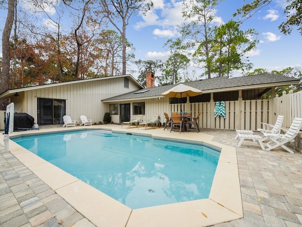 A backyard with a swimming pool, outdoor seating, and a covered patio area.