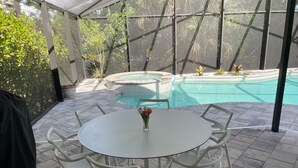 A covered patio area with a pool, a round table with chairs, and potted plants.