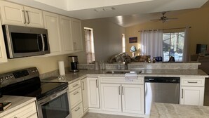 A modern kitchen with white cabinets, stainless steel appliances, and a marble countertop.