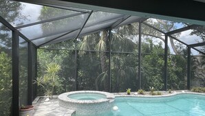 A swimming pool with a glass enclosure, surrounded by potted plants and trees.