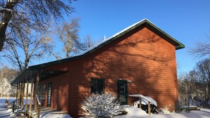 A wooden cabin with a gabled roof, a covered porch, and a snow-covered yard. - 5 BR/2.5 BA Hunting & Fishing Lodge (Watertown)