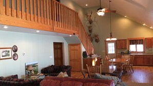 A spacious living area with a high ceiling, a wooden staircase, a dining area, and a kitchen. - 5 BR/2.5 BA Hunting & Fishing Lodge (Watertown)
