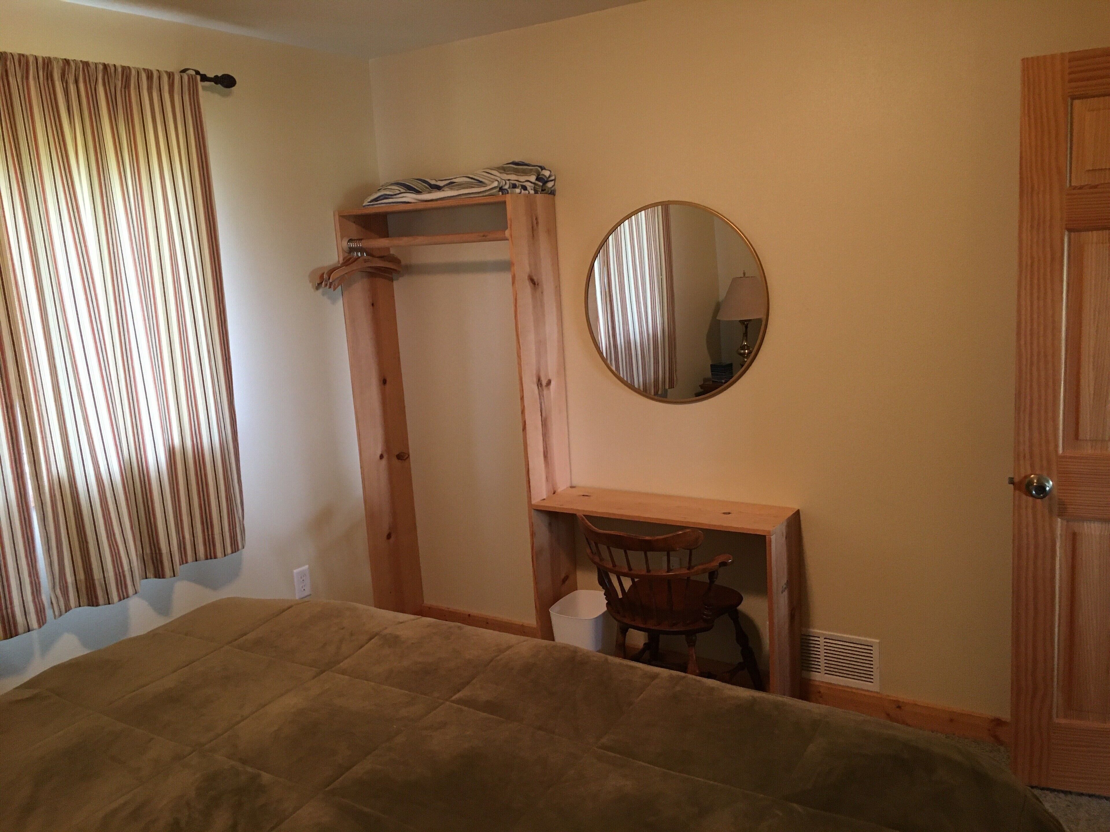 Ein Schlafzimmer mit einem Bett, einem Holztisch, einem Stuhl, einem Spiegel und einem Kleiderschrank.