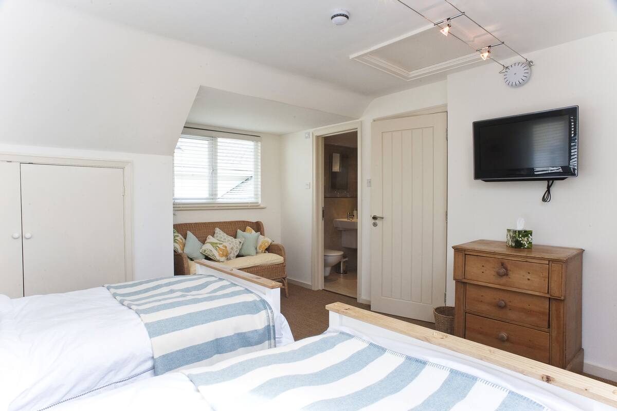 A bedroom with two beds, a television, a wardrobe, and a bathroom visible through an open door.