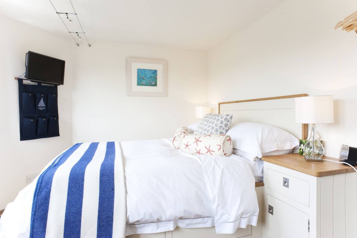 A neatly made bed with a striped blanket, a bedside table with a lamp, and a wall-mounted TV.