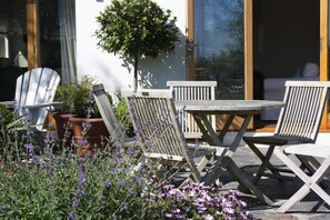 An outdoor seating area with wooden chairs and a table, surrounded by potted plants and purple flowers. - Nearwater B&B (Truro)