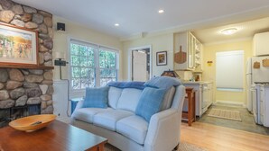 A living room with a stone fireplace, a light blue sofa, a wooden coffee table, and a kitchen in the background.