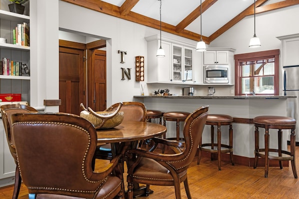 A dining area with a wooden table and chairs, a kitchen with white cabinets and a microwave, and a wooden ceiling with exposed beams. - Private Spacious & Cozy 4 BR-4 Bath Cottage Near Ski Resorts, Northern MI Views (HARBOR SPRINGS)