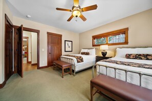 A hotel room with two beds, a ceiling fan, a window with a view, and a door leading to another room.
