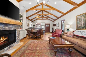 A spacious living room with a fireplace, a dining area, and a kitchen in the background. - Private Spacious & Cozy 4 BR-4 Bath Cottage Near Ski Resorts, Northern MI Views (HARBOR SPRINGS)