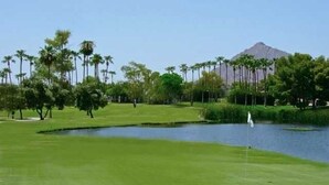 Un parcours de golf avec un étang, des palmiers et une montagne en arrière-plan.