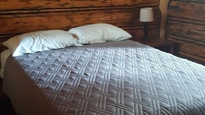 A wooden cabin room with a bed, pillows, and a nightstand with a lamp. - Rustic cabin hidden among the pines. (Condon)