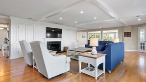 A spacious living room with a fireplace, a blue sofa, a striped armchair, and a small table with a lamp.