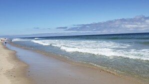 A beach with waves, a clear sky, and a few people walking.