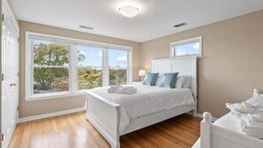 A bedroom with a large window, a bed with white bedding, and a white headboard.