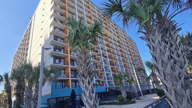 A multi-story hotel with balconies, palm trees, and a clear blue sky. - Beautiful oceanview 1 bedroom with king bed, full kitchen, and water amenities  (Myrtle Beach)