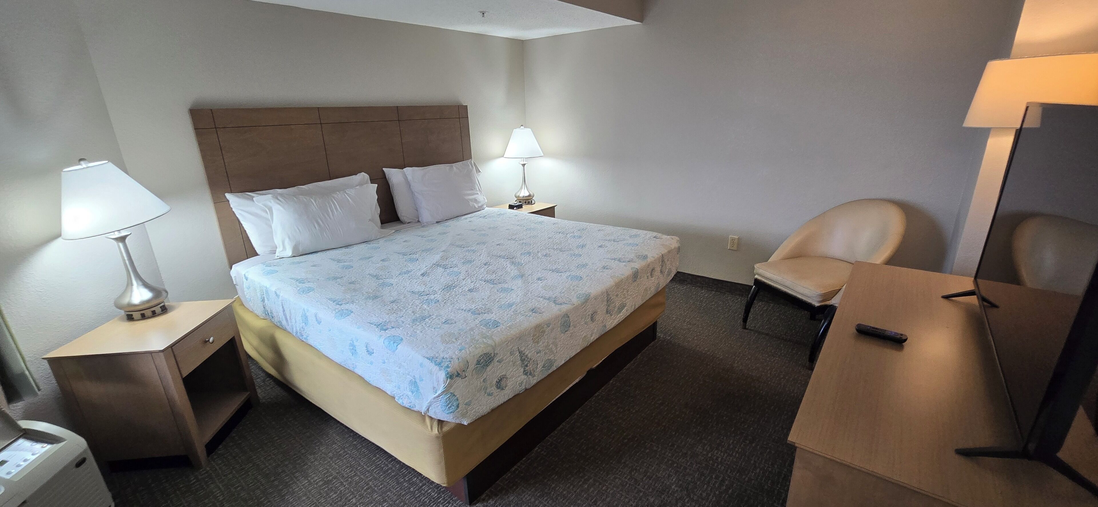 Una habitación de hotel con una cama, dos mesitas de noche con lámparas, una silla y un escritorio.
