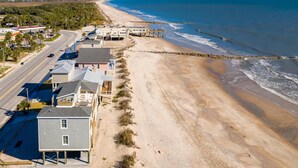 Vue aérienne d’une zone côtière avec une plage, une route et des bâtiments le long du littoral.