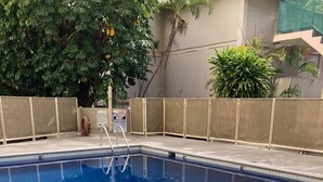 Ein rechteckiger Pool mit klarem, blauem Wasser, umgeben von einer Fliesenveranda und einer niedrigen Steinmauer.