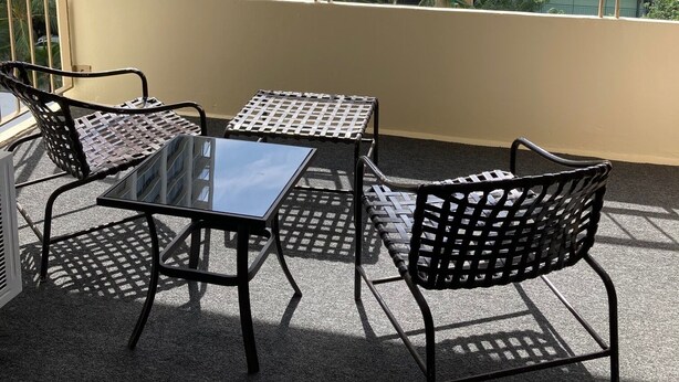 Ein Balkon mit Tisch und zwei Stühlen, mit Blick auf ein mehrstöckiges Gebäude mit Balkonen und einem klaren Himmel.