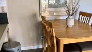Ein Essbereich mit Holztisch, sechs Stühlen, einer Vase mit Zweigen und einem großen gerahmten Bild an der Wand.