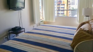 Ein Hotelzimmer mit Bett, Fernseher auf einem Tisch, einem Fenster mit Vorhängen und einer Lampe auf einem Nachttisch.