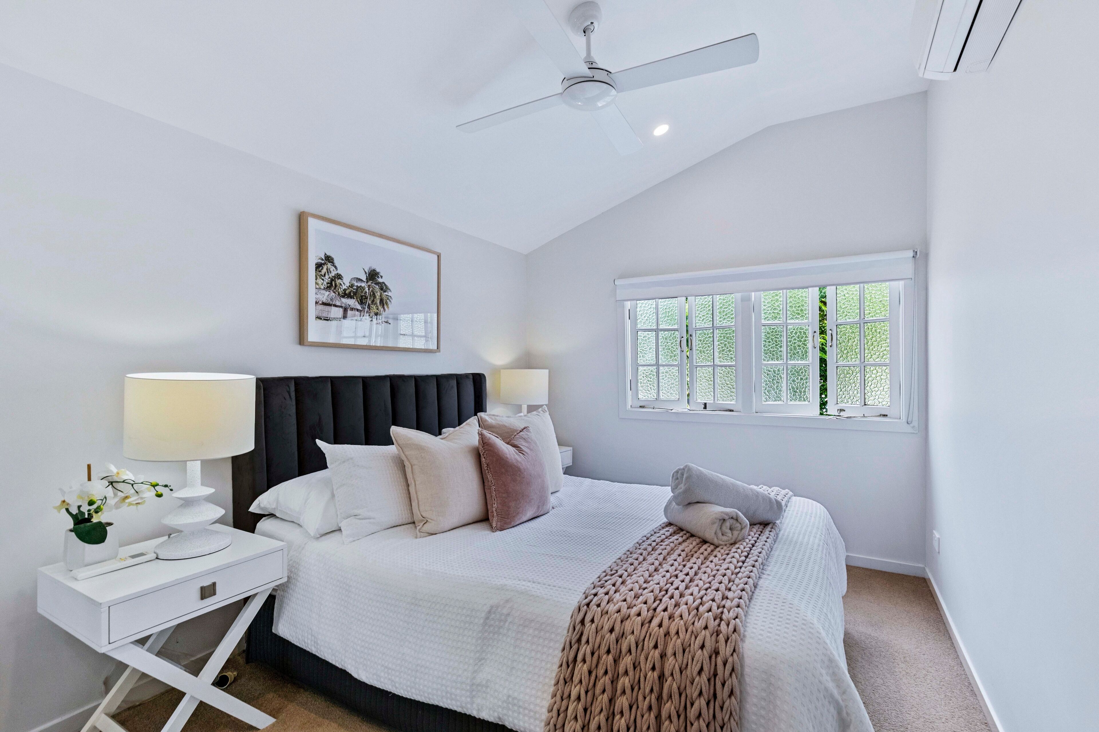 A bedroom with a bed, nightstands, a ceiling fan, a window, and a framed picture on the wall.