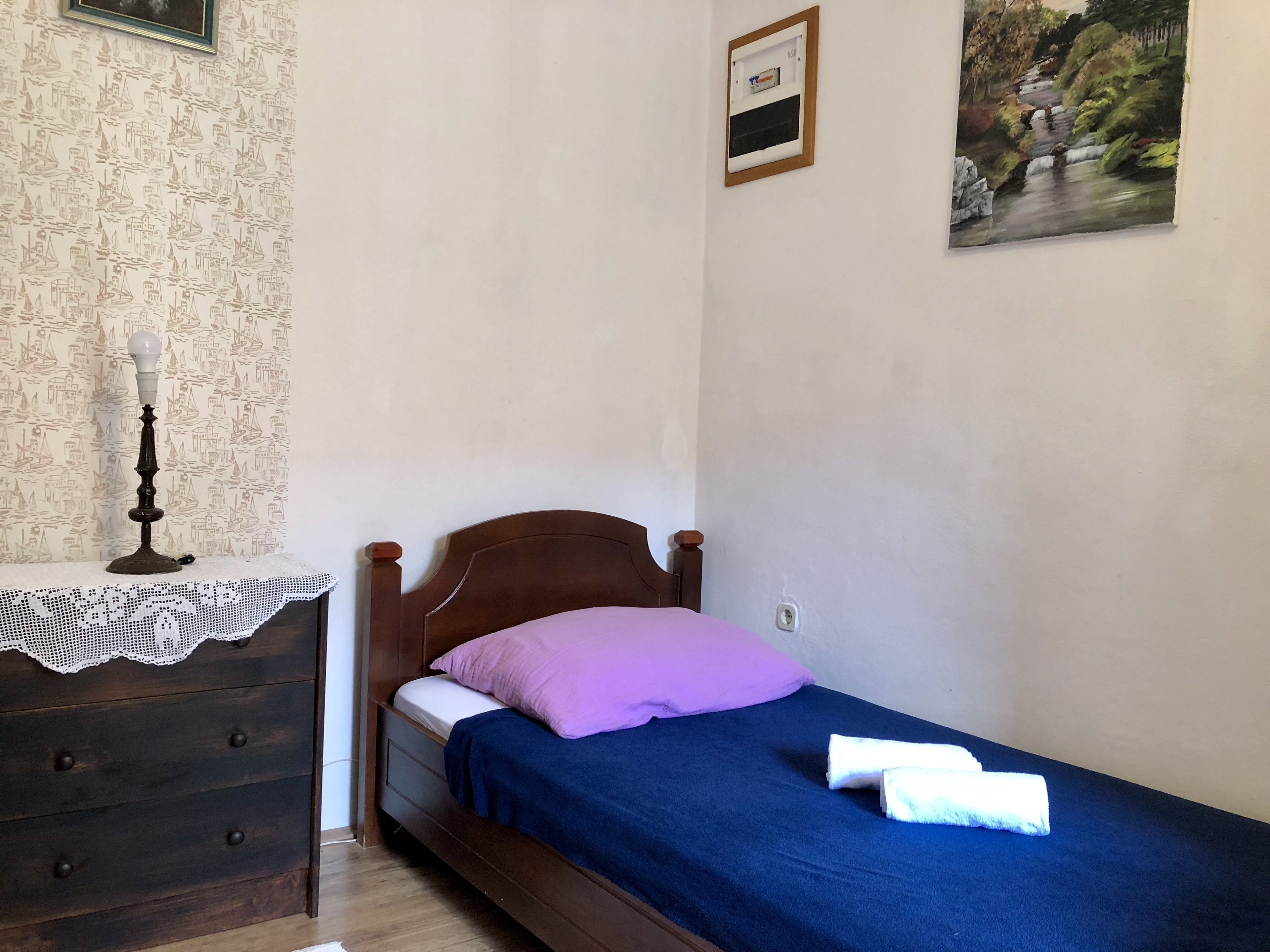 A small, neatly arranged bedroom with a single bed, a dresser, and a nightstand.