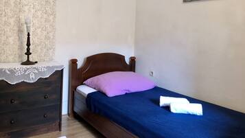 A small, neatly arranged bedroom with a single bed, a dresser, and a nightstand.