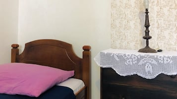 A bedroom with a wooden bed, a pink pillow, a white blanket, a lace tablecloth, and a wall with a nautical pattern.