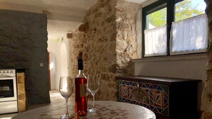 Un muro de piedra, una mesa redonda con una botella y dos vasos, y un armario con azulejos.