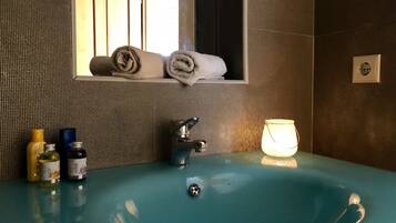 A bathroom with a teal sink, a mirror, and a window. There are towels stacked in the mirror, a soap dispenser, and a glass jar on the sink.