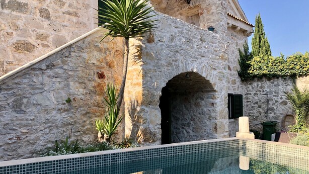 Un edificio de piedra con una piscina con azulejos en primer plano.