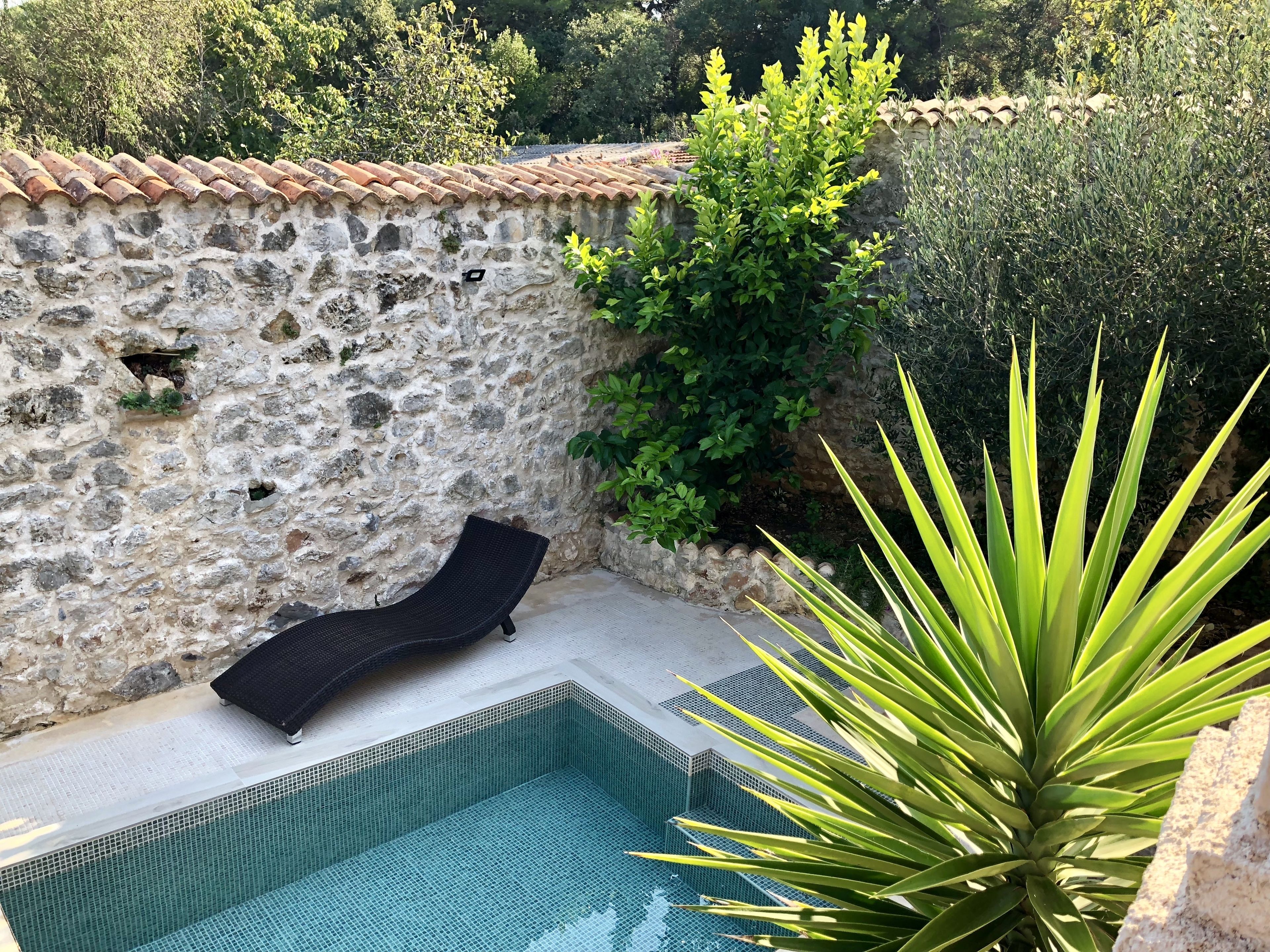 A stone wall with a tiled roof, a black lounge chair, and a swimming pool.