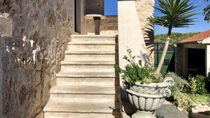 Una escalera de piedra que conduce a un edificio con una pared de piedra rústica y una gran maceta decorativa con plantas.