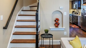 A staircase with wooden steps and a black handrail, leading to a living area with a white sofa and a small table with a plant.