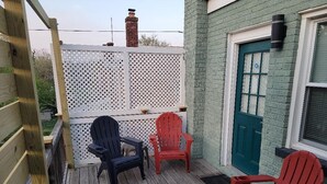 A wooden deck with two Adirondack chairs, a white lattice fence, and a teal door.