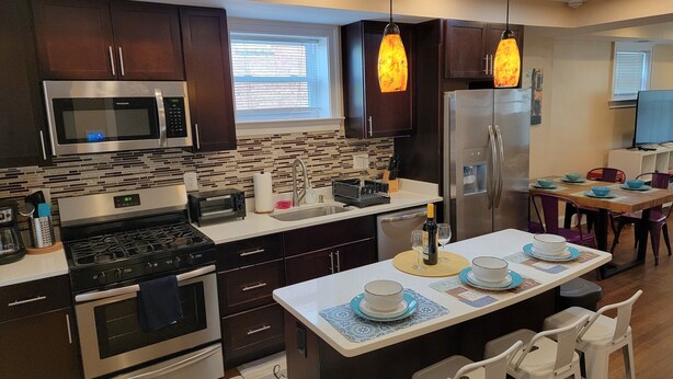 A modern kitchen with dark wooden cabinets, stainless steel appliances, a central island with bar seating, and pendant lighting.