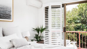 A bedroom with a bed, pillows, a bedside table, a lamp, a potted plant, and a window with a view of greenery. - A PERFECT STAY - Cooinda  (Byron Bay)
