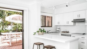 A modern kitchen with white cabinetry, a large island, and a view of the outdoor patio area. - A PERFECT STAY - Cooinda  (Byron Bay)