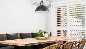 A dining area with a wooden table, wicker chairs, and a black pendant light. - A PERFECT STAY - Cooinda  (Byron Bay)
