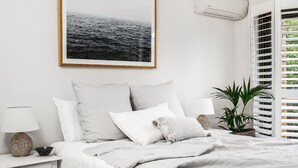 A bedroom with a bed, white bedding, a framed picture on the wall, a bedside lamp, a potted plant, and a window with blinds. - A PERFECT STAY - Cooinda  (Byron Bay)