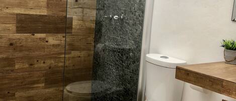 A bathroom with a shower, toilet, and wooden flooring.